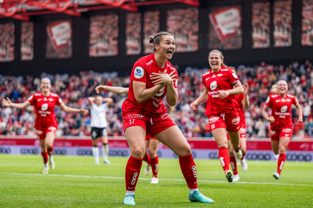 Branns Anna Aahjem feirer sin avgjørende scoring mot Rosenborg i Toppserien 2024, på Brann Stadion. Marthine Østenstad og øvrige Brann-spillere stormer mot henne for å feire.